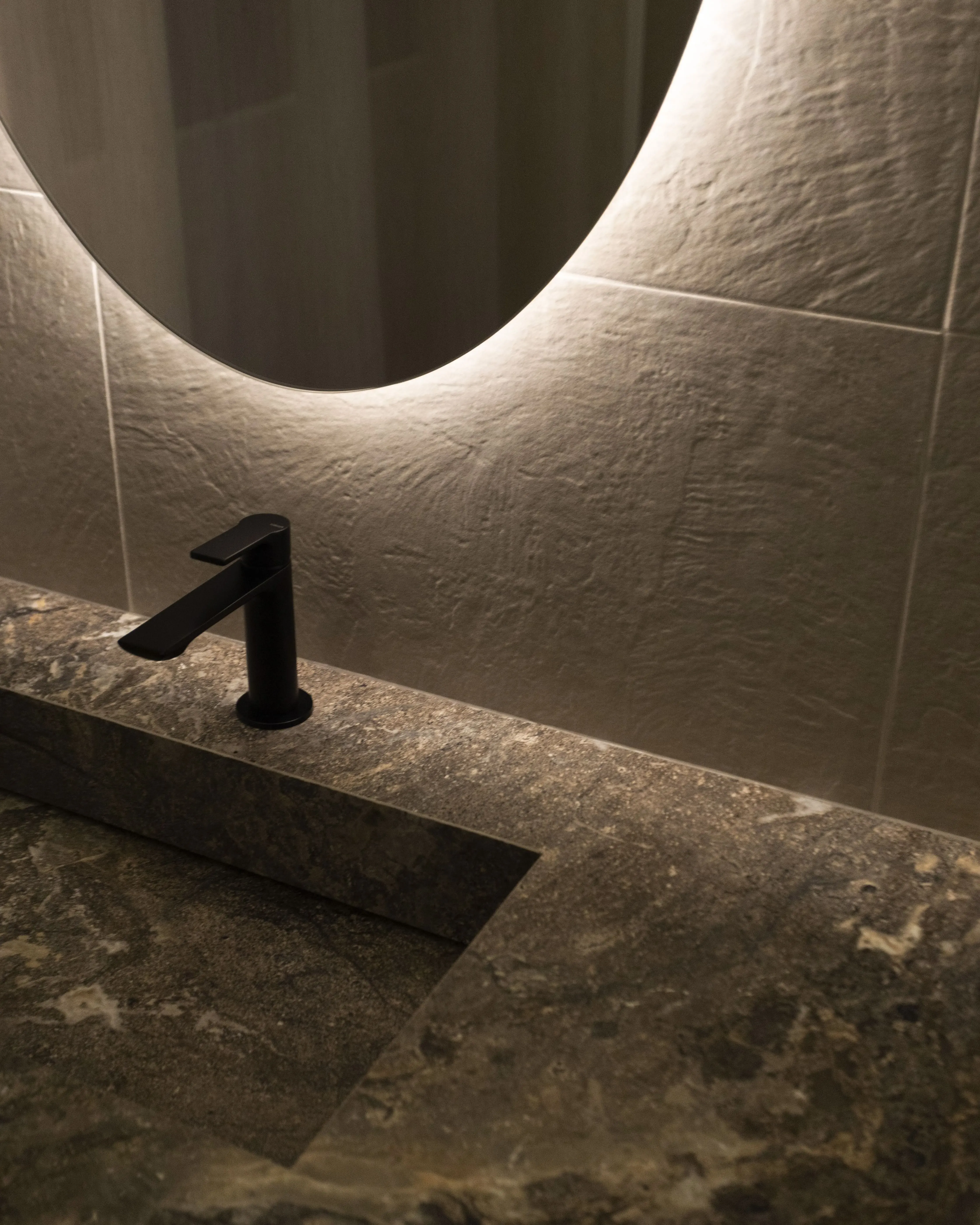 Dettaglio di un bagno finito: lavabo in pietra, rubinetteria nera e specchio retroilluminato